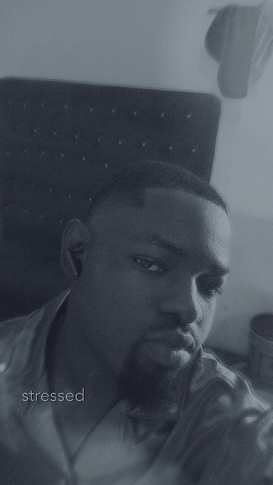 A black-and-white filtered selfie of a man looking tired or contemplative, with the word 'stressed' written in the bottom left corner.