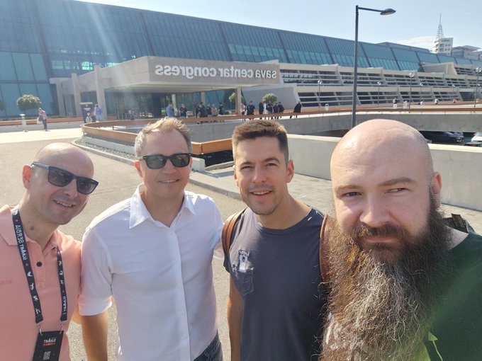 Four men smile for a selfie in front of the Sava Centar Congress building, with the reversed text "sava centar congress" visible on the glass facade behind them, as they arrive for Solana Summit Serbia.