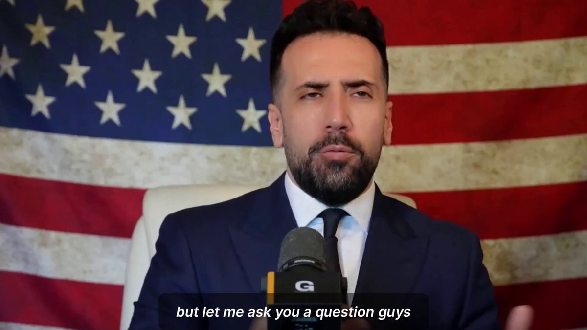 The image features a man dressed in a suit, sitting behind a microphone with his hands on his lap. The background includes an American flag, which adds context to the setting of the scene. The caption below the image reads "Let me ask you a question guys".