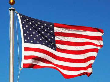 The American flag waves against a clear blue sky, symbolizing the U.S. government's potential to finally establish clear regulations for the cryptocurrency industry through the CLARITY Act. The image evokes patriotic anticipation for legislative progress on crypto rules.