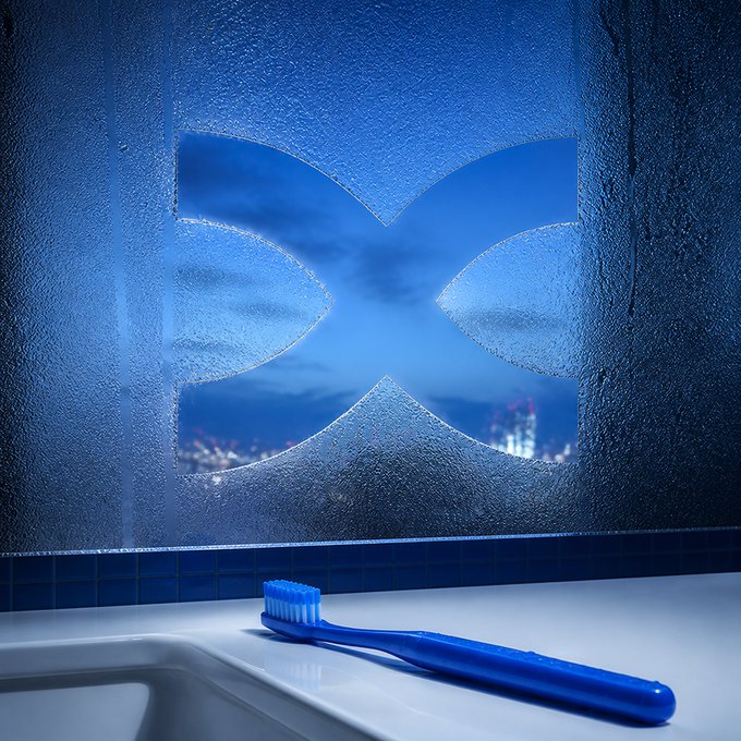 A blue toothbrush rests on a bathroom counter in front of a fogged mirror with the "X" (Twitter/X logo) wiped clear to reveal a cityscape, visually linking a morning routine to the market routine of checking X for financial news.