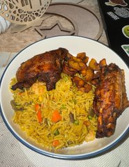 A plate of yellow rice pilaf served with grilled chicken pieces and ribs in a dark sauce, garnished with vegetables.