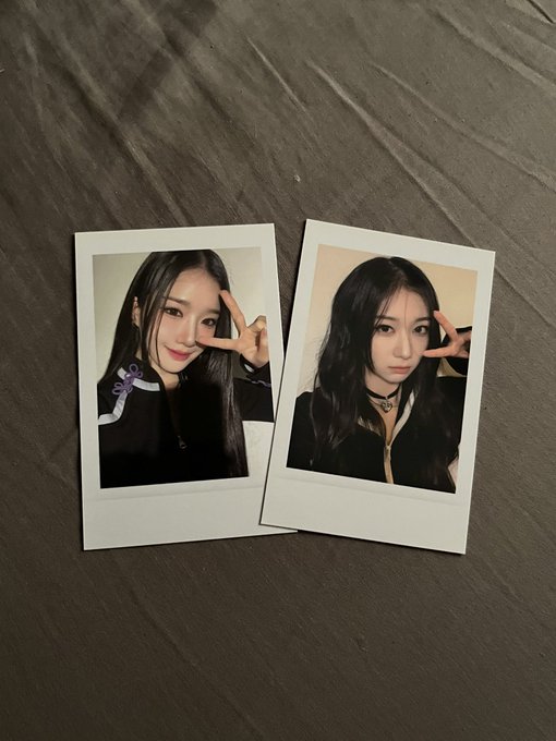 Two polaroid photos lie on a wooden surface, both showing young women with long dark hair making peace signs.