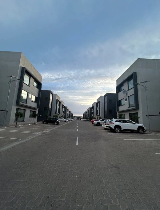 A wide shot of an empty residential street lined with modern, two-story townhouses under a cloudy sky at dusk.