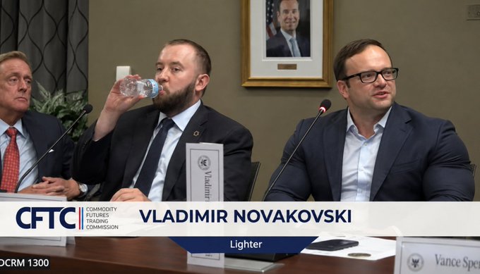 Three men in suits sitting at a panel during a CFTC (Commodity Futures Trading Commission) hearing, with the man in the center drinking from a water bottle and a nameplate reading 'Vladimir Novakovski, Lighter' in front of him.