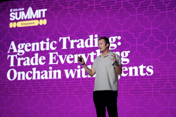 A man in a light button-up shirt speaks on stage at the Solana Summit Singapore, with the presentation title "Agentic Trading: Trade Everything Onchain with Agents" displayed on a vibrant purple backdrop behind him.