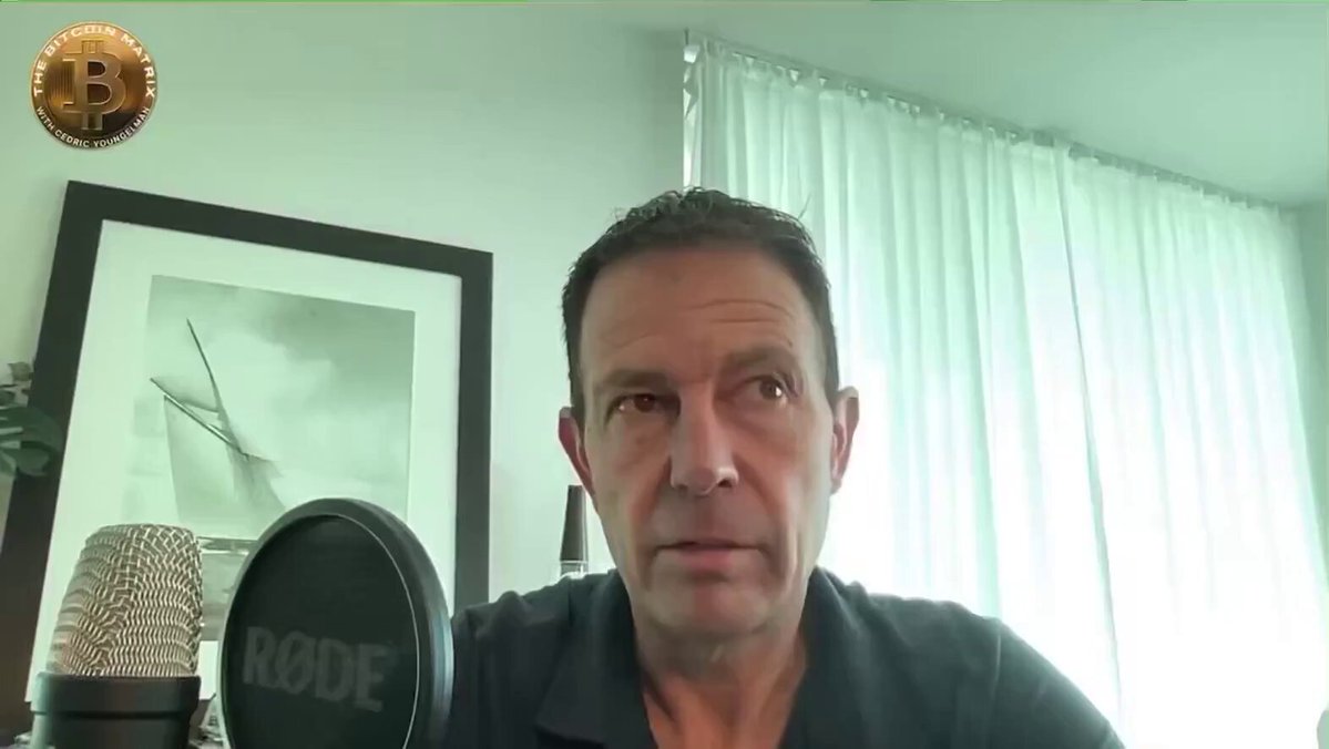 The image features a man sitting at a microphone with a gold coin placed behind him. The caption above the image reads, "Jeff booth said, 'Anytime you're measuring Bitcoin in the piece of paper, you're still in the system of control.'". This statement is related to the Bitcoin post because it highlights how Bitcoin operates within a financial system that relies on digital currency and can be easily measured. The man's presence behind the microphone suggests he might be speaking or presenting about Bitcoin at an event or conference.