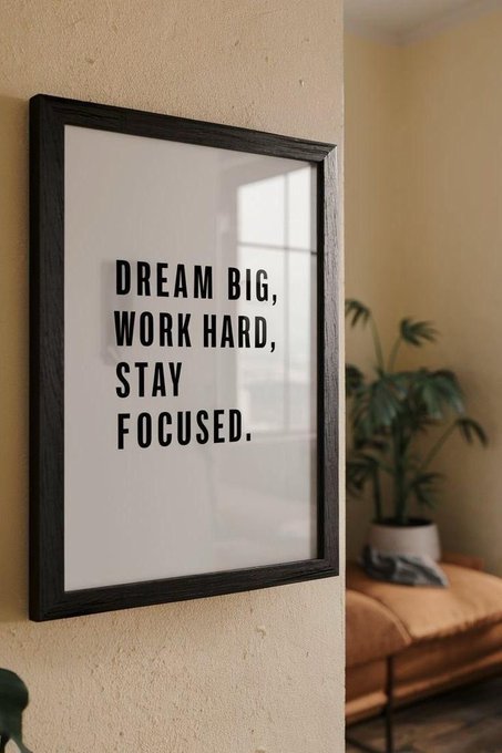 A framed black-and-white motivational poster on a beige wall reads 'DREAM BIG, WORK HARD, STAY FOCUSED.' next to a potted plant.