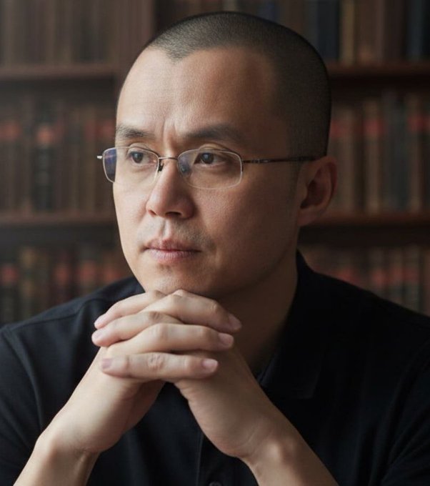 The image features a man with glasses sitting at a desk or table, wearing a black shirt. He has his hands crossed over each other as he looks off into the distance. The background includes bookshelves filled with various books, suggesting that this scene takes place in a library or a similar setting where people can be found reading and studying.

The image also contains text that reads "Binance founder CZ says, Bitcoin won'n't be dead for too long." This quote is attributed to the man sitting at the desk with his hands crossed over each other. The phrase "Don't panic" is also present in the image, which could be interpreted as a reminder not to worry about the uncertain future of Bitcoin or any other investments.