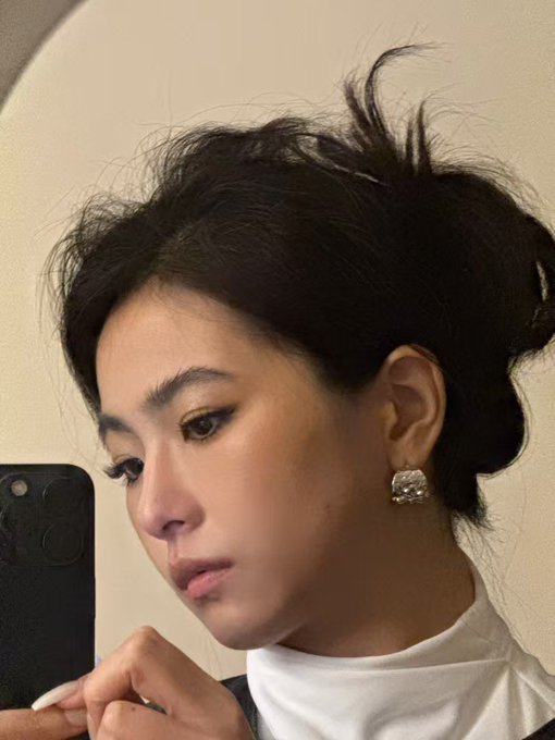 The image features a woman with her hair styled in an updo, wearing earrings that include a pendant design. She appears to be taking a selfie using her cell phone, capturing her reflection in the mirror. The caption of the photo reads "Successfully introduced me to a match 5BNB".