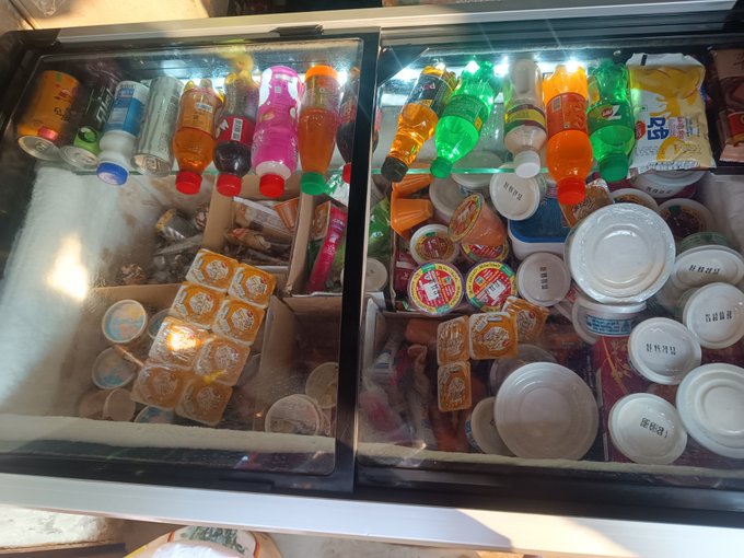 Two glass-top freezers filled with assorted ice cream tubs, popsicles, and bottled drinks in a convenience store or shop.