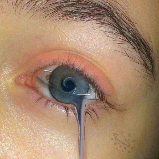 A close-up of a person's eye with artistic digital editing that makes the iris appear to melt or drip downward like liquid, accompanied by a small tattoo design of a planet and stars on the cheek.