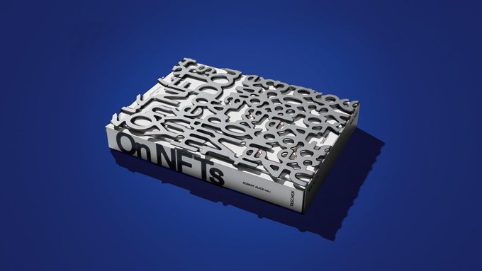 A white Taschen Collector's Edition book titled "On NFTs," featuring an intricate typographic cover design, rests on a dark blue surface, representing the special edition that has been acquired by major art museums worldwide for their collections.