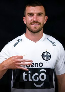 A portrait of soccer player Lionel Messi wearing a white and black striped Olimpia jersey with sponsors 'tigo' and 'epicbet' visible, gesturing with his hand.