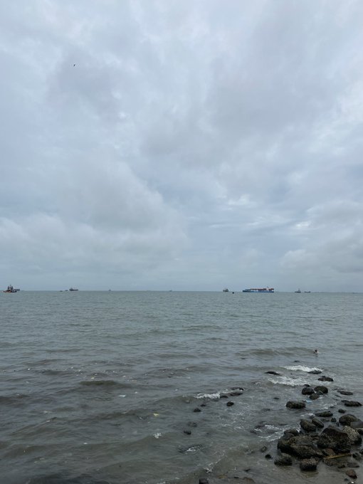 An overcast seascape shows cargo ships anchored far out on the horizon, with rocky shoreline in the foreground and gentle waves lapping the coast. The Vietnamese caption plays on the phrase "xa bờ" (far from shore), humorously comparing the photographer's emotional distance from friends to the distant ships still anchored at sea, while joking that crypto trader "Sol" is finally seeing trading volume as Vietnamese users begin deploying.