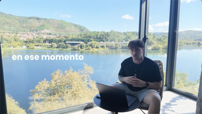 A young man sitting by a window overlooking a scenic lake with mountains and a bridge, with Spanish text overlay reading 'en ese momento'.