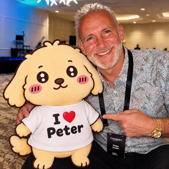 A smiling older man with gray hair poses with a cartoon dog pillow wearing a shirt that reads 'I ❤ Peter', and his name tag says 'Peter Speer'.