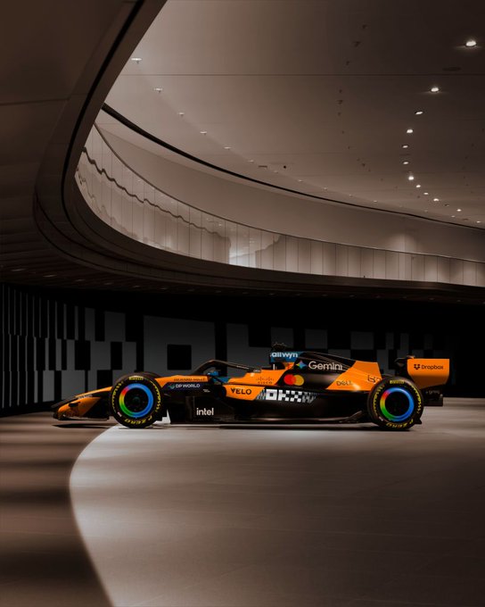 A sleek McLaren Formula 1 car is displayed in a modern showroom, featuring prominent sponsor logos including OKX, Gemini, Dell, Intel, Dropbox, and DP World. The image showcases the car's new livery, tying into the post's mention of a "new whip" with McLaren F1.