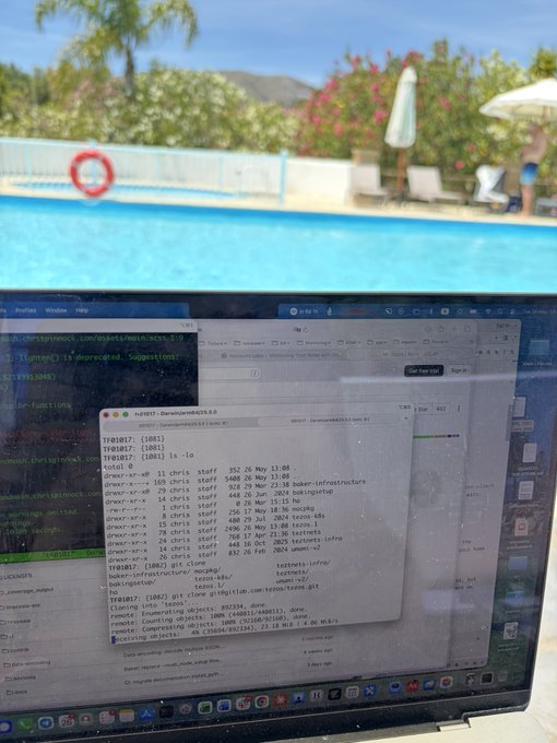 The image shows a laptop screen displaying a webpage with information about the Tezos project, which appears to be related to a swimming pool or outdoor setting. The text "Just cloning the Tezos sources by the pool" suggests that someone has been using their computer to replicate the source code of the Tezos project onto another device, possibly for educational purposes or personal interest.