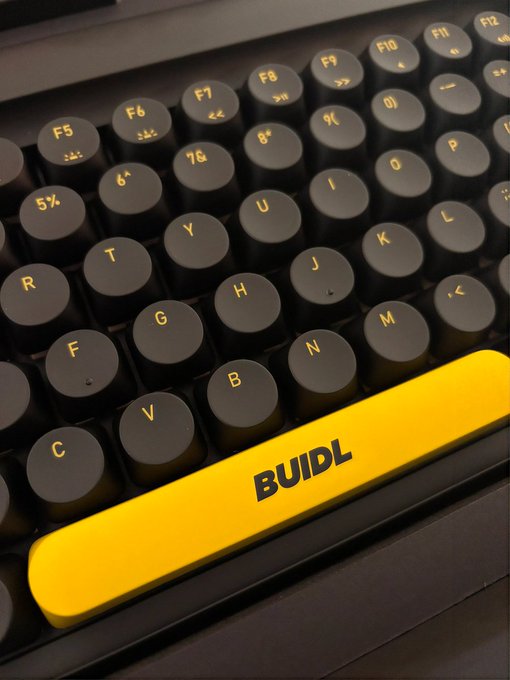 A close-up of a vintage-style typewriter keyboard with round black keys and a bright yellow spacebar labeled 'BUIDL'.