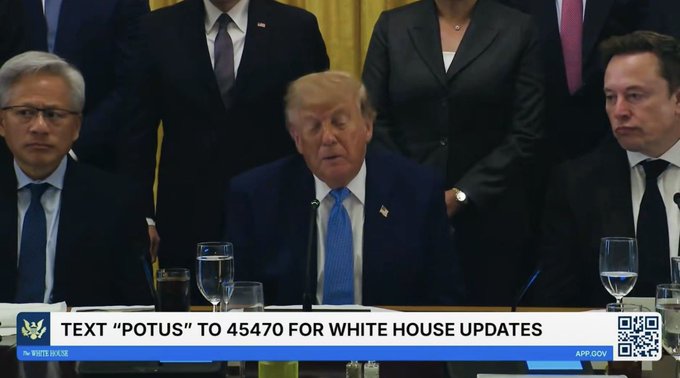 A White House scene showing Donald Trump speaking at a table, flanked by Jensen Huang (left) and Elon Musk (right), with a chyron reading "TEXT 'POTUS' TO 45470 FOR WHITE HOUSE UPDATES" and "WHITE HOUSE".