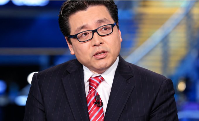 A man wearing a dark pinstripe suit, red and white striped tie, and glasses appears to be speaking in a broadcast or interview setting.