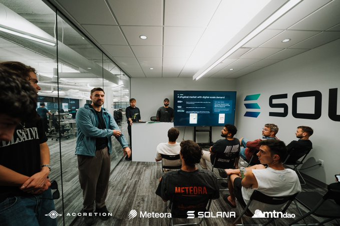 A group of attendees gathers in a modern conference room featuring Solana branding on the wall, listening to a presentation titled "A physical market with digital-scale demand" displayed on screen, representing the Meteora x Solana partnership event on on-chain collectibles and digital packs. Logos for Accretion, Meteora, Solana, and mtndao are visible at the bottom, capturing the collaborative workshop atmosphere described in the post.