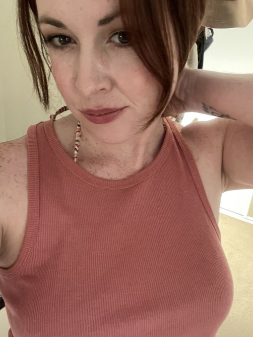 A close-up selfie of a woman with freckles, short brown hair, and a rust-colored ribbed tank top.