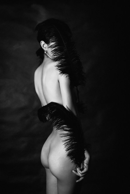 A black and white image features a person posing with large black feathers, available on Opensea for 0.05 ETH as a 1/1 piece.