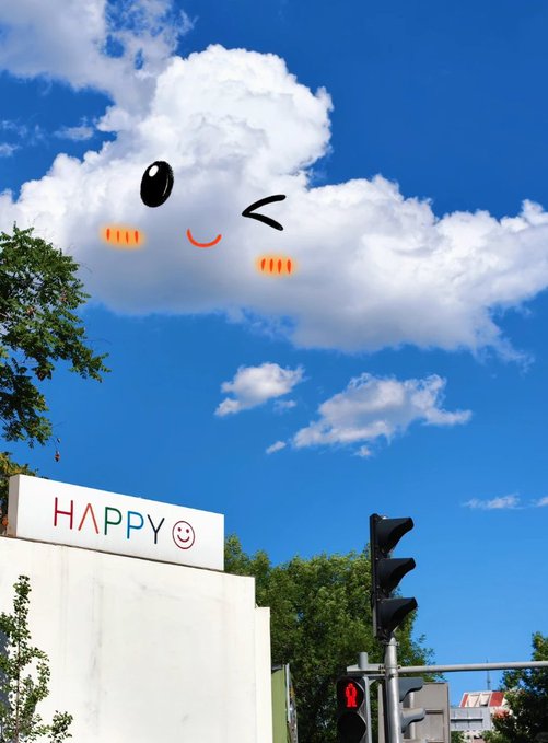 An outdoor photo showing a blue sky with white clouds where a cute face has been digitally added; below is a wall with the text 'HAPPY' and a smiley face next to a traffic light.