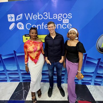 Three people posing together in front of a blue backdrop for the 'Web3Lagos Conference 5.0', with a woman in an orange top, a man in a dark jacket, and a woman in a black top and purple pants.