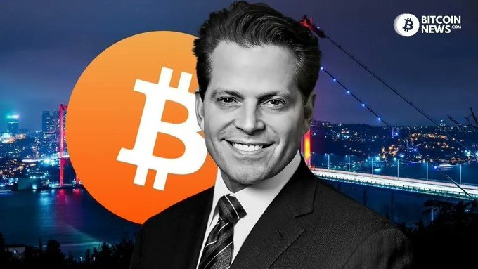 Anthony Scaramucci, shown smiling in a suit with a Bitcoin logo and illuminated bridge backdrop, comments on how veteran Bitcoin holders ("OGs") sold after reaching the $100K milestone they had long awaited. The image, branded with BitcoinNews.com, visually reinforces his remarks about early investors cashing out at this psychologically significant price point.
