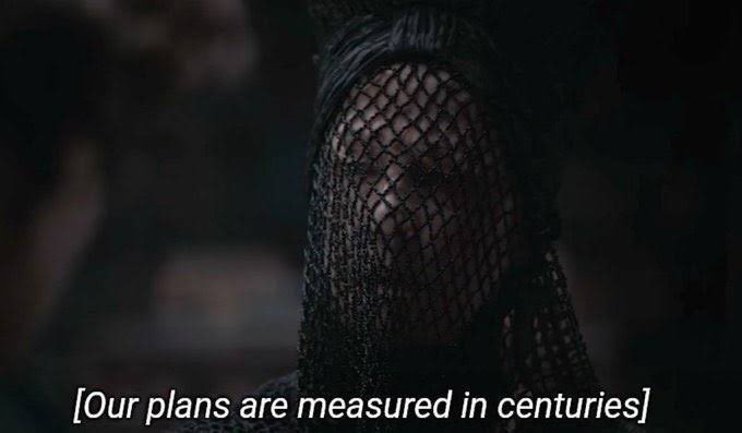 The image features a person wearing a black headdress with a mesh netting over their eyes. Below the image, there is text that reads "Your plans are measured in centuries", which suggests that the person's actions or decisions might have long-lasting consequences. The image also includes a caption about the value of an item being $10,000 one day.