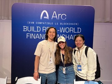 Three members of the Arc team smile in front of an "Arc (EVM Compatible L1 Blockchain) - Build Real-World Finance onchain" banner at ETHGlobal NYC, where they hosted a hackathon offering 15,000 USDC in prizes across six tracks for builders developing applications like stablecoin logic and prediction markets.