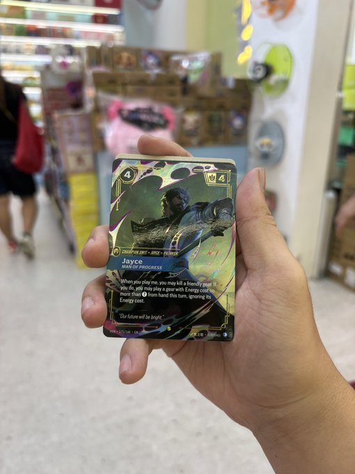 A hand holding a holographic trading card of 'Joyce, Maid of Progress' (Champion Unit - Void - Pirate) with a cost of 4, photographed inside a brightly lit store.