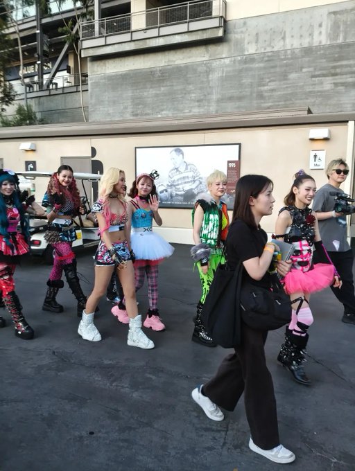 A group of fans in colorful, eye-catching outfits walk together outside what appears to be a 1995 event venue, waiting for XG to arrive. The scene captures the excitement of XTRA XG HITC fans, though, as the caption humorously notes, "soon" from XG often translates to several months of waiting.
