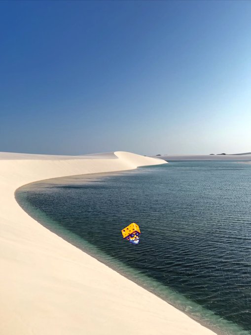A scenic landscape showing white sand dunes meeting calm turquoise water under a clear blue sky, with a small SpongeBob SquarePants sticker overlaid.