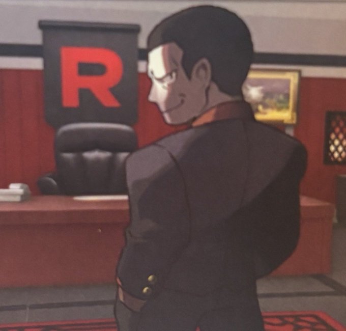 An animated character in a black suit smirks while standing in an office featuring a large red 'R' banner on the wall.