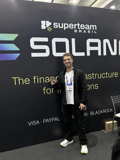 A man stands in front of a black Solana 'Superteam Brasil' backdrop at a crypto event, with sponsor logos including Visa, PayPal, and BlackRock visible.