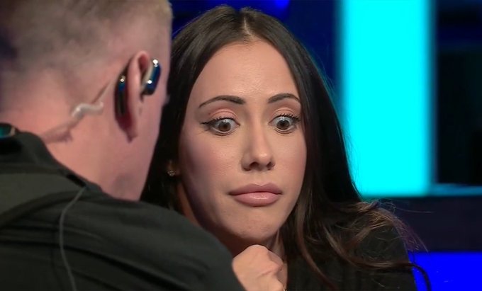 A woman with dark hair and wide eyes stares intensely in surprise at a man wearing an earpiece, set against a blue studio background. The "wide-eyed surprise" expression humorously conveys the unexpected arrival of the weekend, fitting the caption about being "onchain on a Friday night."