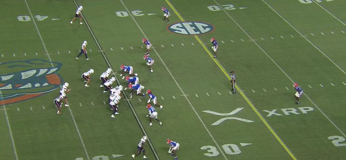 An overhead view of an American football game in progress on a green turf field marked with yard lines, the SEC logo, and XRP branding, with players lined up at the line of scrimmage.