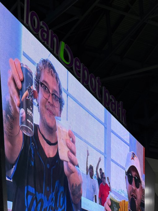 A large digital billboard at loanDepot park showing a man with glasses and tattoos holding a beer and food, smiling at the camera.