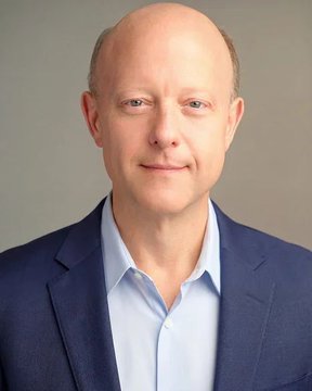 A professional headshot of a bald middle-aged man in a navy blue blazer and light blue collared shirt, smiling slightly at the camera against a gray background, likely representing an executive at Circle. The accompanying post discusses Circle receiving final OCC approval to become a federally regulated trust bank under Circle National Trust.