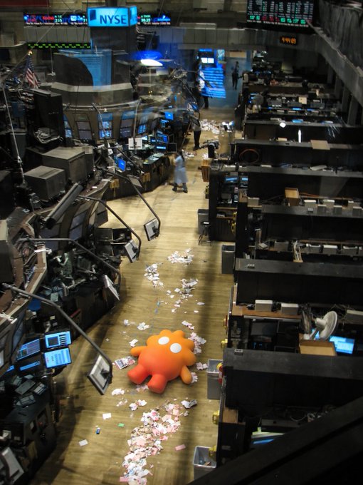 An edited image shows the floor of the New York Stock Exchange (NYSE) covered in paper, with a large orange cartoon octopus lying in the middle of the trading floor.