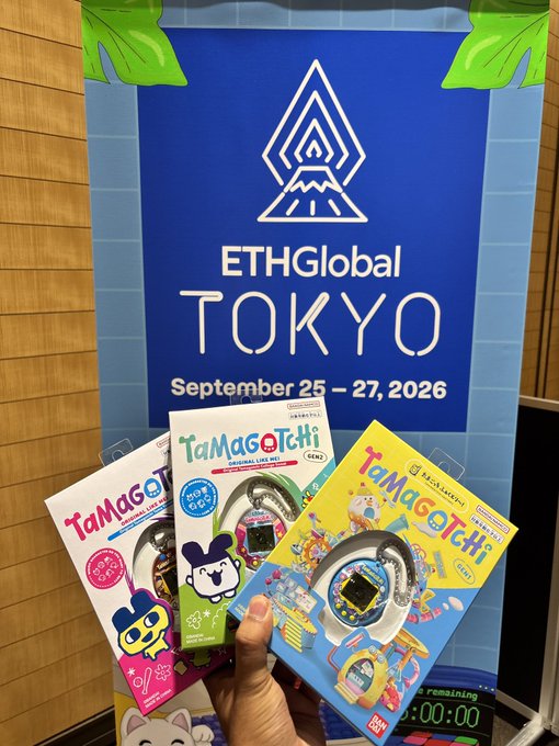 A hand holds up three Tamagotchi Original Live Mix devices in front of an 'ETHGlobal TOKYO September 25-27, 2026' event banner. The Tamagotchis feature pink, black mouse, and yellow character designs.