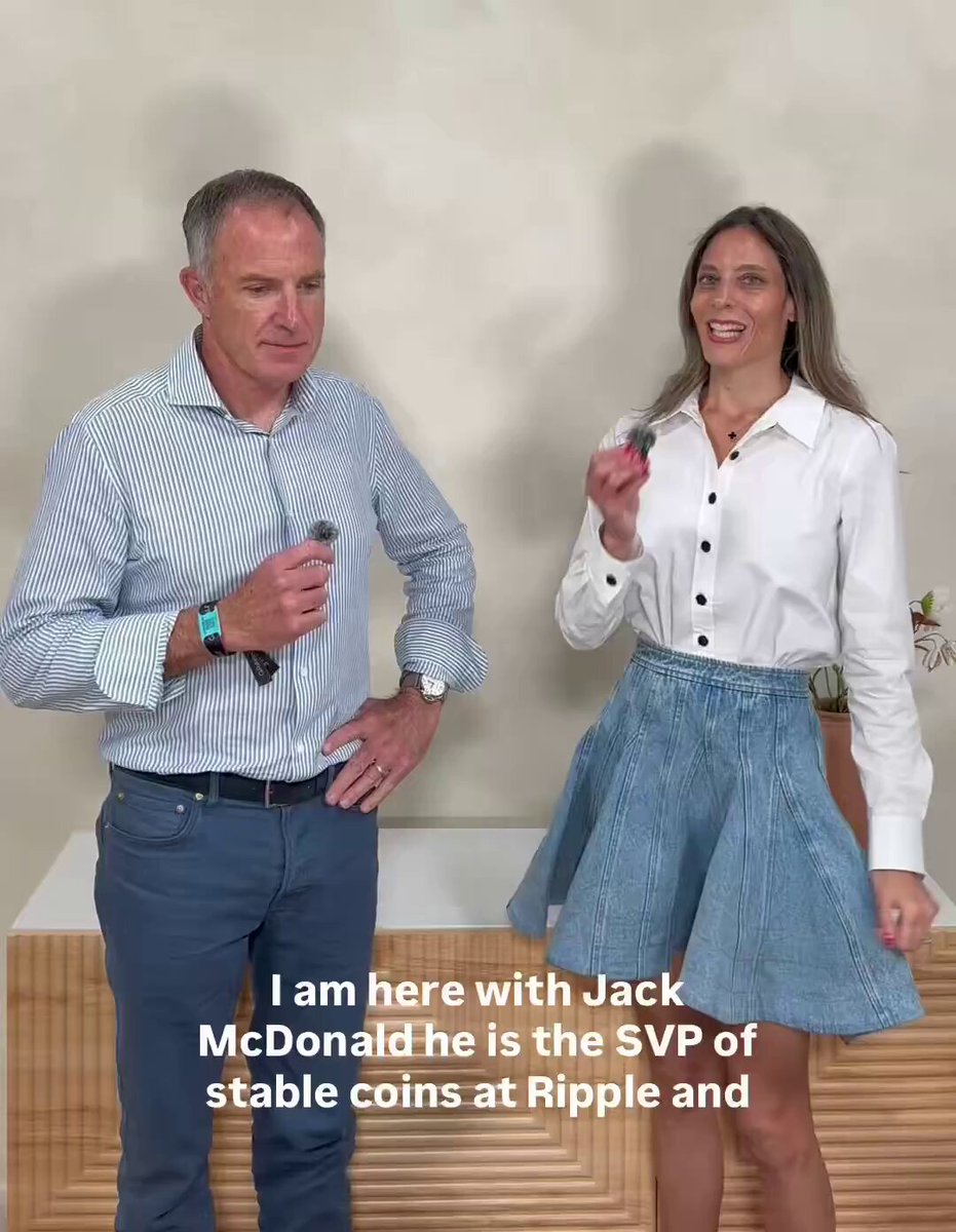 The image features a man wearing a blue striped shirt and jeans, standing next to a woman who is dressed in a white shirt and blue skirt. The man appears to be holding a microphone while they both smile at each other. The background of the image shows a wooden wall with text that reads "Ripple SVP of stablecoins, Jack McDonald, explains that RLUSD is a top 5 USD backed stablecoin, noting that the average daily activity is well ahead of expectations. Trading volume is up and RLUSD launched on OKX for spot and derivatives trading". The post seems to be discussing the stability and potential growth of Ripple SVP's stablecoins, specifically focusing on the stability of the Ripple SVP token (RLDN).