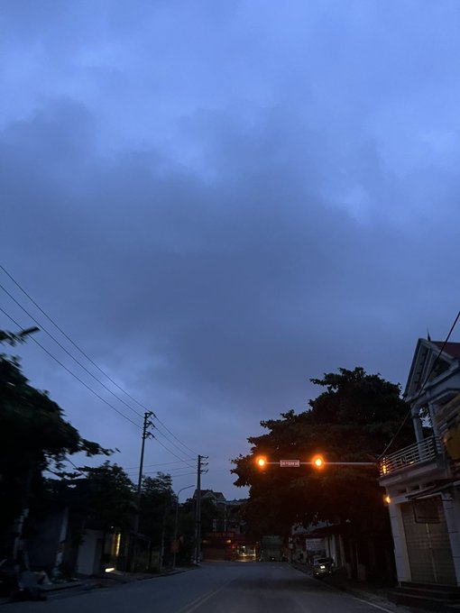 An evening photograph captures a quiet street scene under a deep blue cloudy sky, with a traffic light glowing red and a "Do Not Enter" sign visible in the distance.