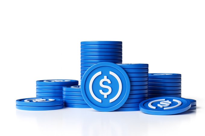 A pile of blue USDC tokens featuring the dollar sign symbol, representing the stablecoin's dominance in capturing roughly 70% of adjusted stablecoin transaction volume compared to USDT's 25% in H1 2026.