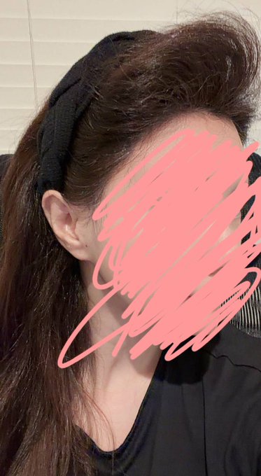 A close-up selfie of a person with long brown hair and a black headband, with their face scribbled out in pink.