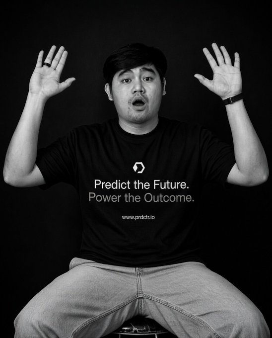A black-and-white photo shows a surprised man with his hands raised, wearing a t-shirt that reads 'Predict the Future. Power the Outcome. www.prdctr.io'.